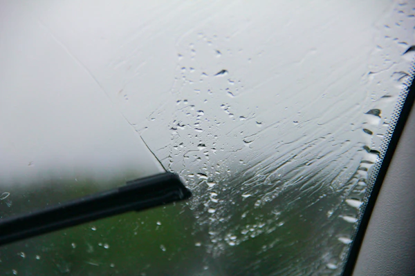 A sleek windshield wiper blade resting against a car windshield with raindrops