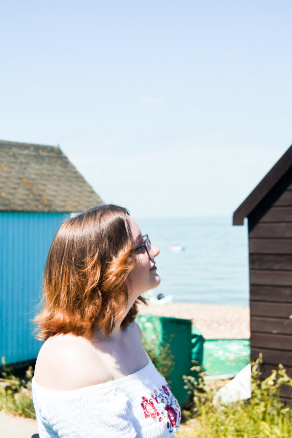 Mujer con camiseta blanca sin mangas con gafas de sol mirando la casa de madera azul durante el día