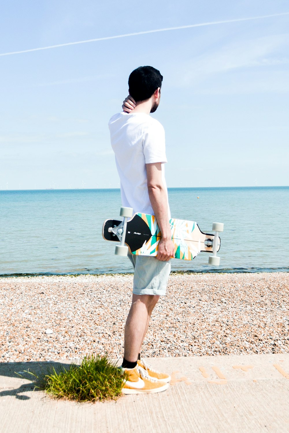 Homme en t-shirt blanc et short blanc portant un sac à dos noir et blanc debout sur un brun