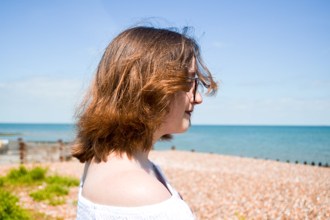 woman in white tank top standing on brown sand near body of water during daytime