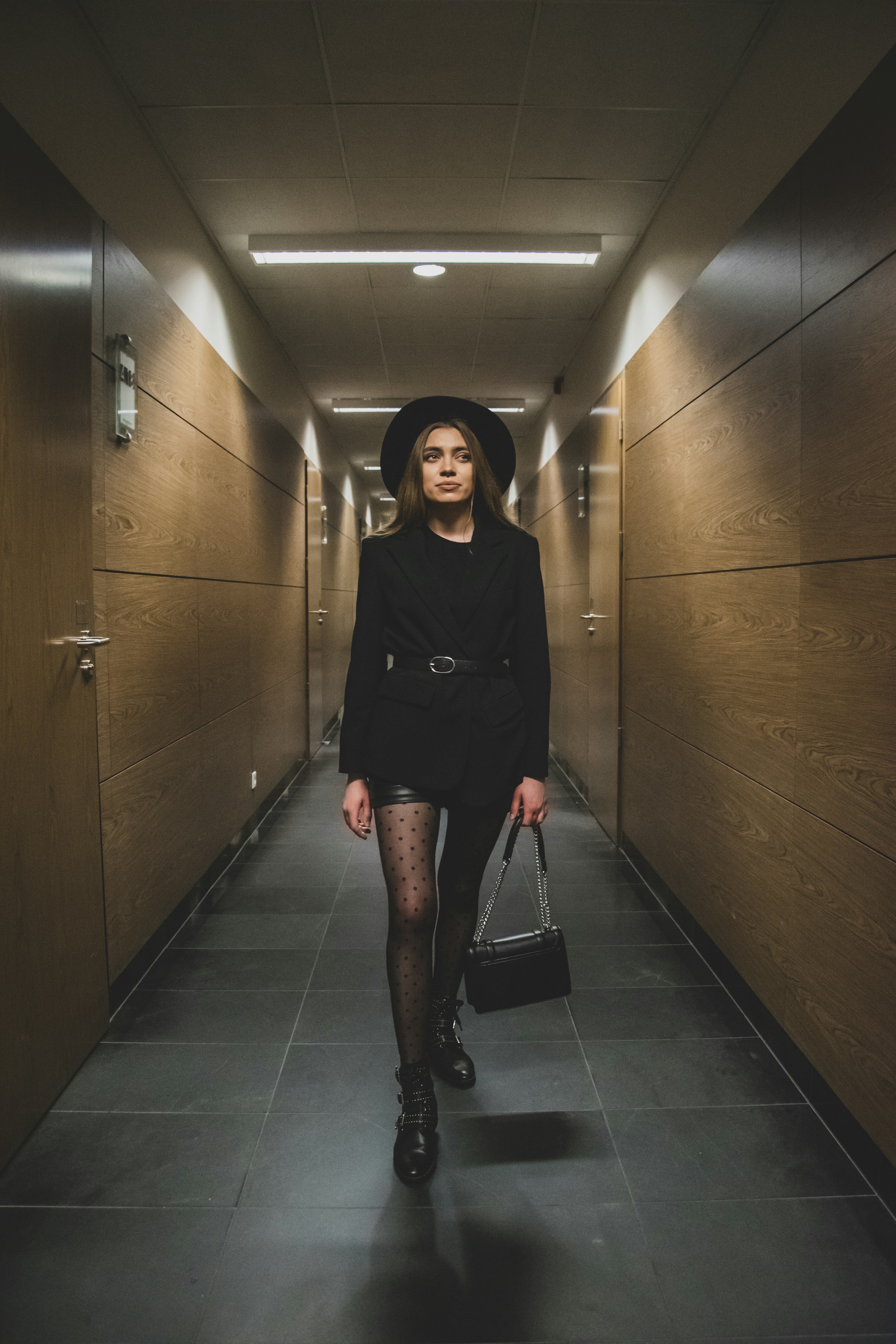 Una mujer con un vestido negro y sombrero caminando por un pasillo
