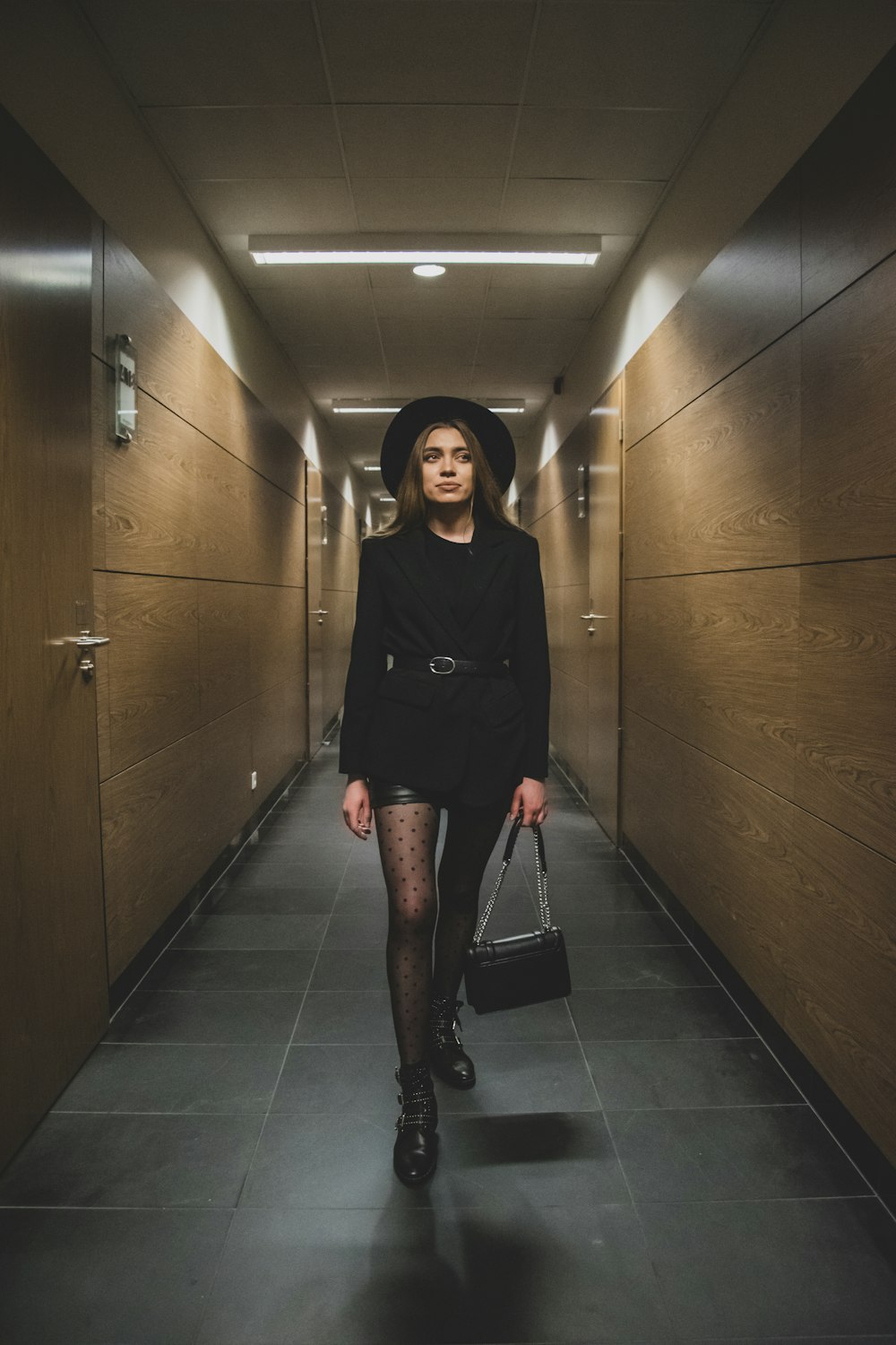 Eine Frau in schwarzem Kleid und Hut geht einen Flur entlang