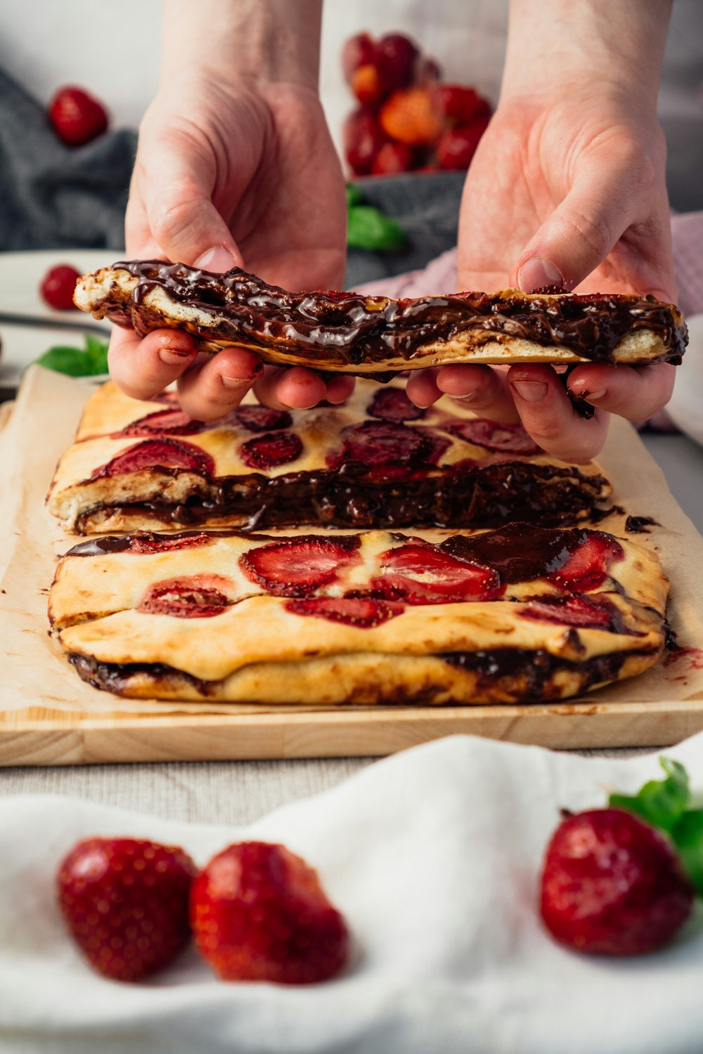 a person holding a pastry with chocolate and strawberries on it
