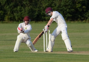man in white jersey shirt and white pants holding baseball bat on green grass field during