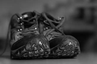 A pair of rugged hiking boots is placed side by side on a surface, showcasing their sturdy soles with visible treads designed for outdoor terrain. The laces are tied neatly, and the boots appear well-used, suggesting they have been worn for many adventures.