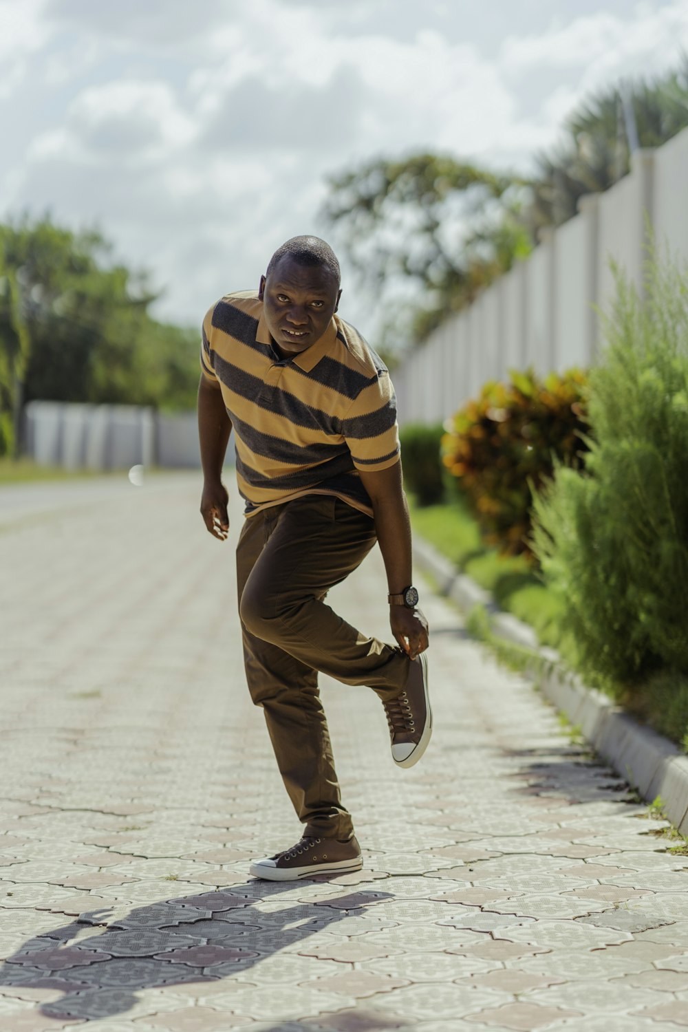 man in yellow and black stripe polo shirt and brown pants sitting on concrete pathway during