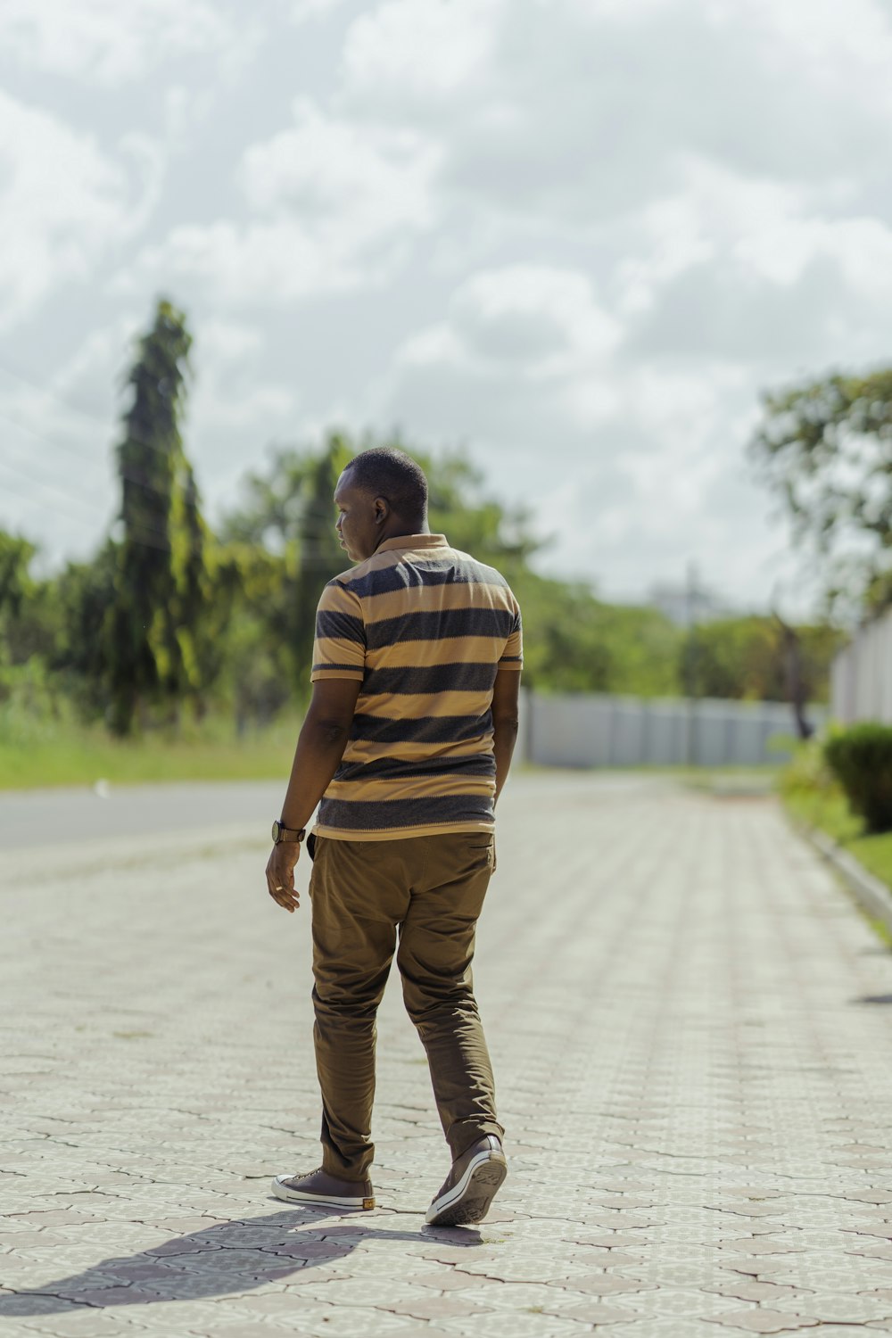 man in brown and white stripe polo shirt and brown pants walking on gray sand during