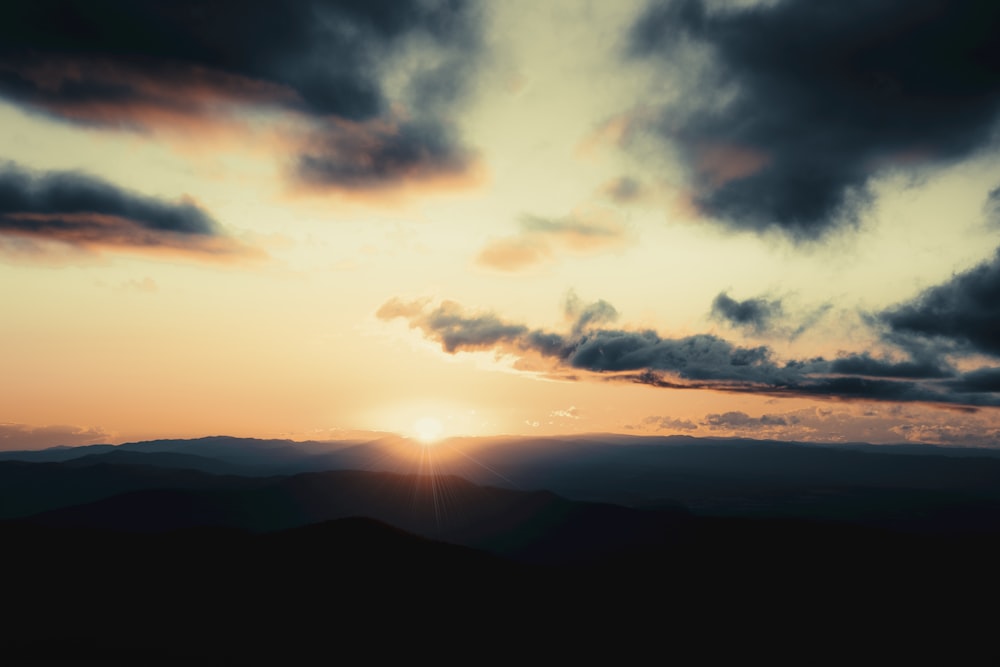 silhouette of mountains under cloudy sky during sunset