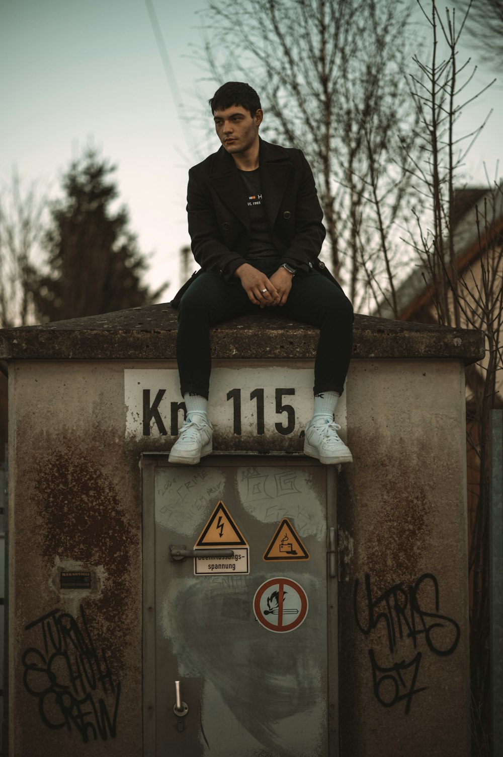 man in black jacket sitting on gray concrete wall