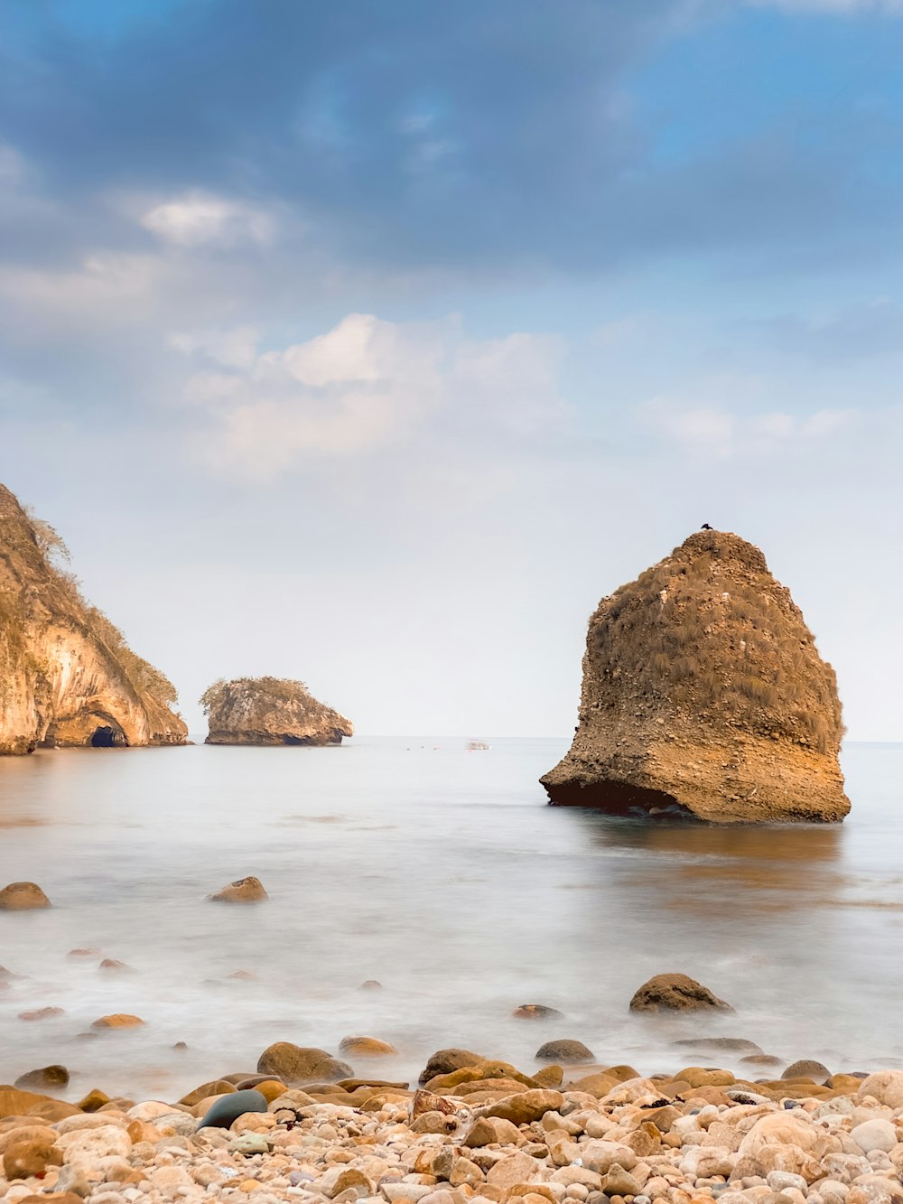 a rocky beach with two large rocks sticking out of the water