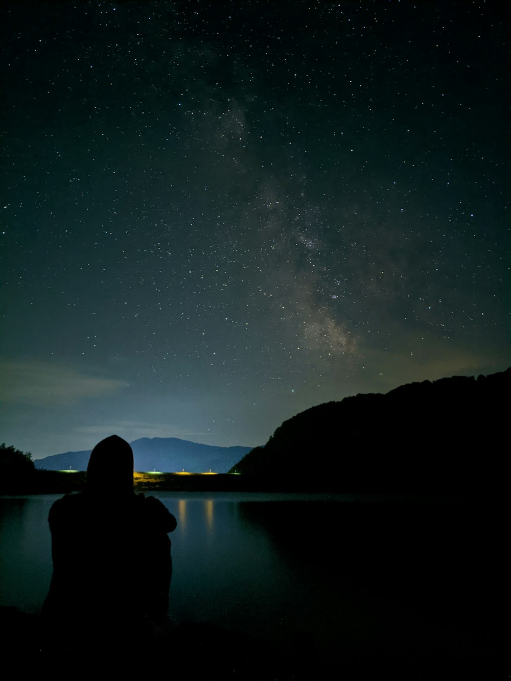 silhouette of person sitting on rock near body of water during night time