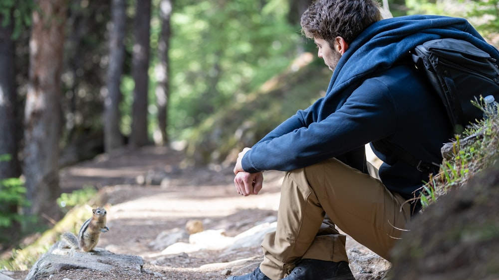man in blue hoodie and brown pants sitting on gray rock during daytime