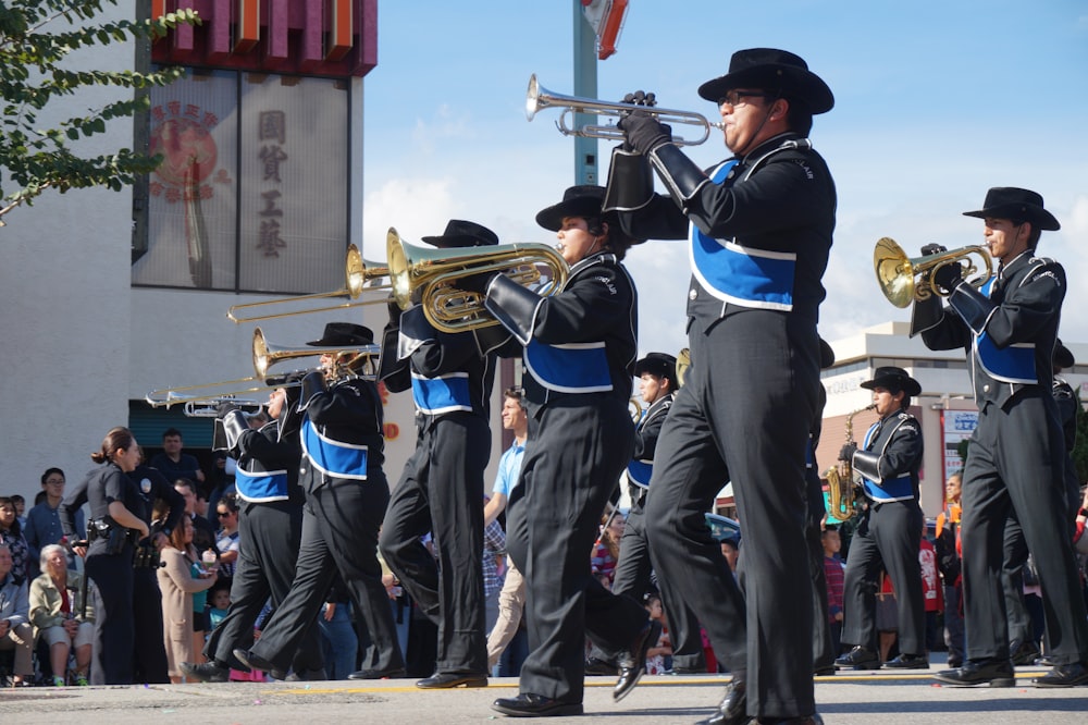 Personas con uniforme negro y azul tocando instrumentos musicales durante el día