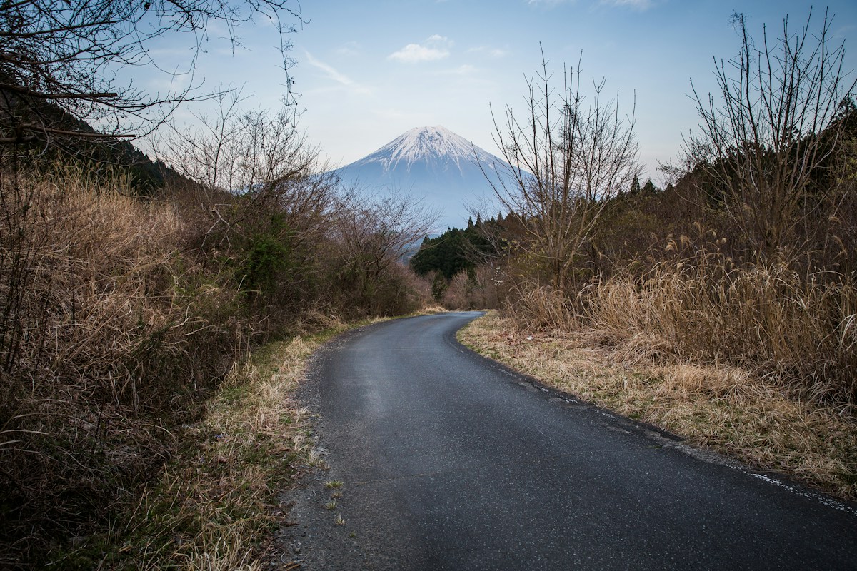 A two-lane road curving towards snow-capped Mount Fuji in the distance