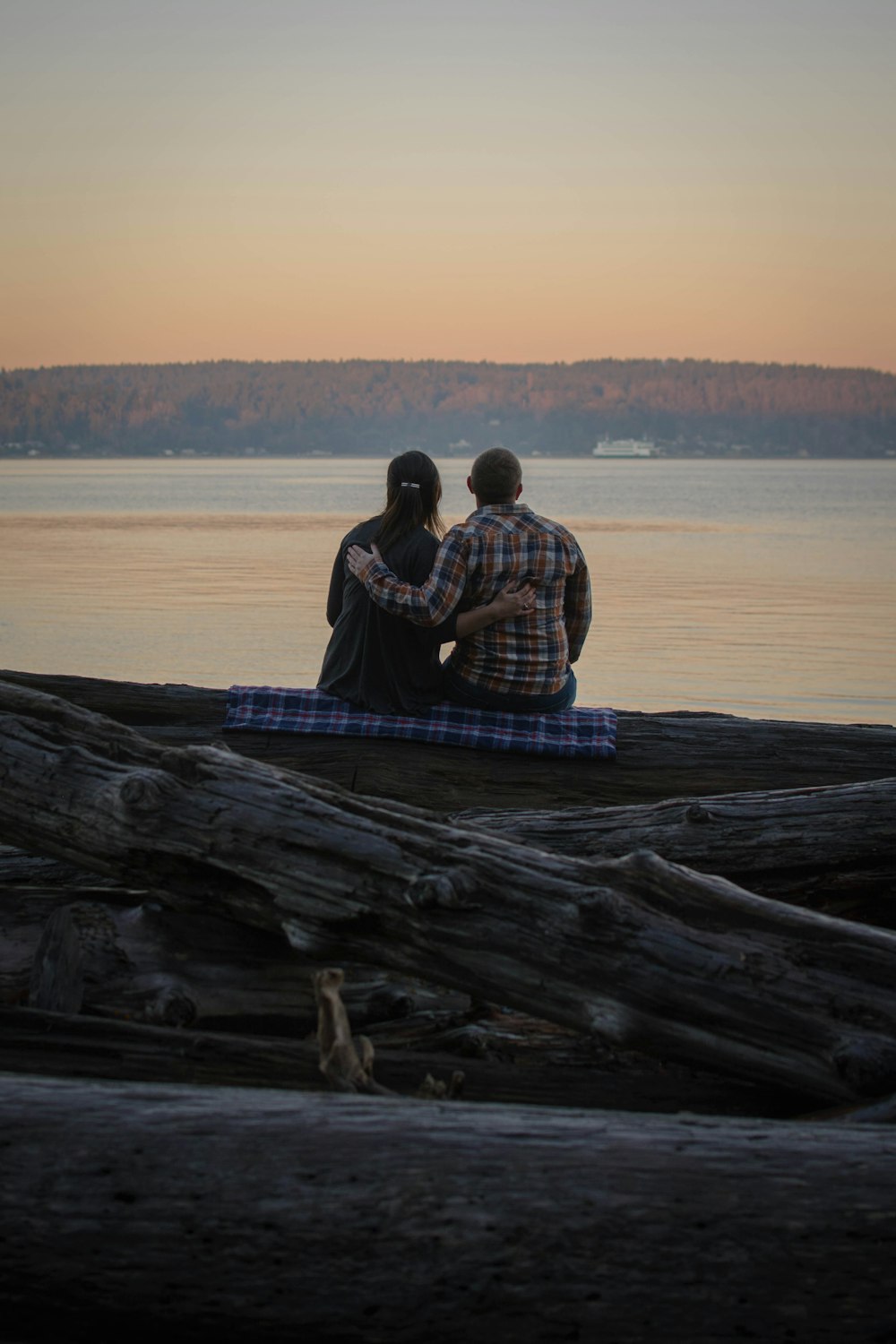 two people sitting on a log looking out at the water