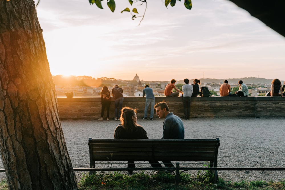 two people sitting on a bench near a tree