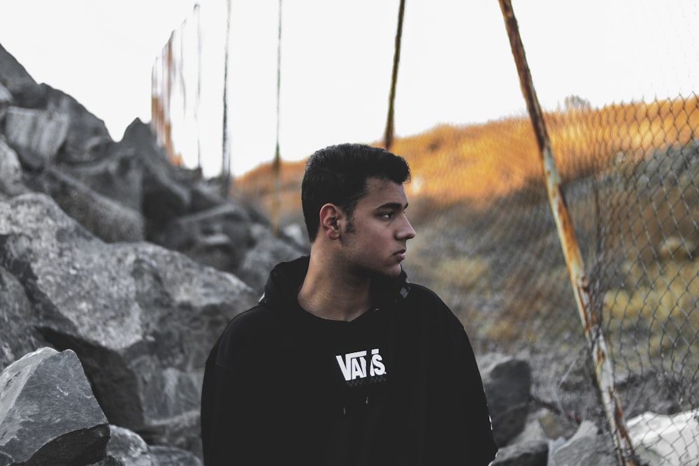 man in black hoodie standing near brown metal fence during daytime