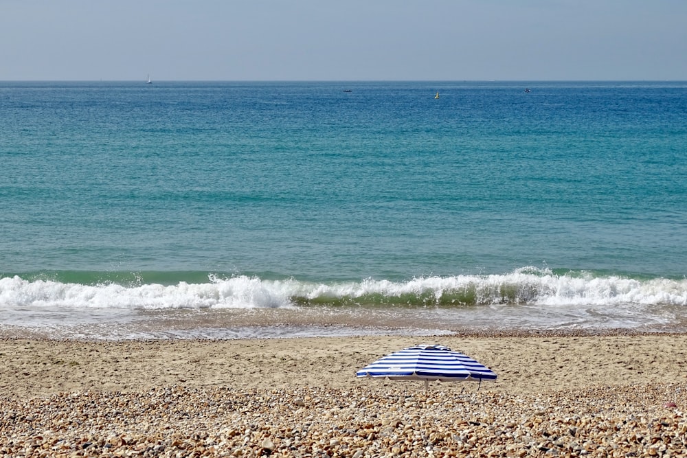 a blue and white umbrella sitting on top of a sandy beach