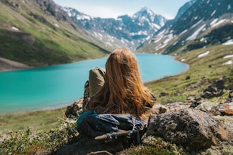 a woman sitting on a rock looking at a lake