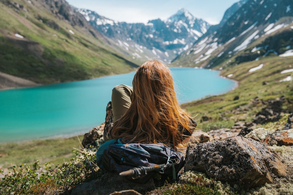 Eine Frau, die auf einem Felsen sitzt und auf einen See schaut