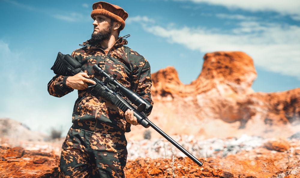 a man in camouflage holding a rifle in the desert