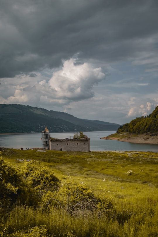 white and brown concrete building near body of water under white clouds during daytime in Mavrovo North Macedonia