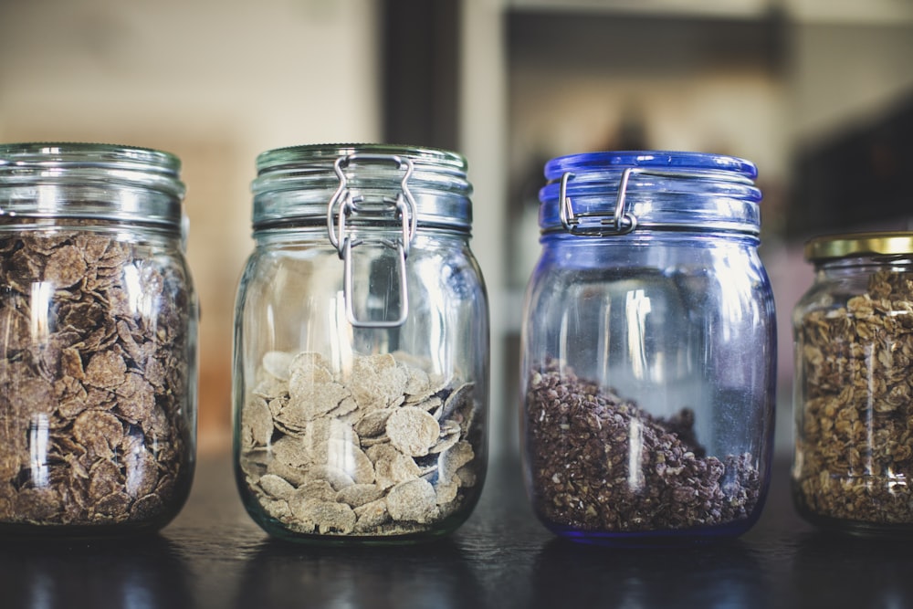 four glass jars filled with different types of food