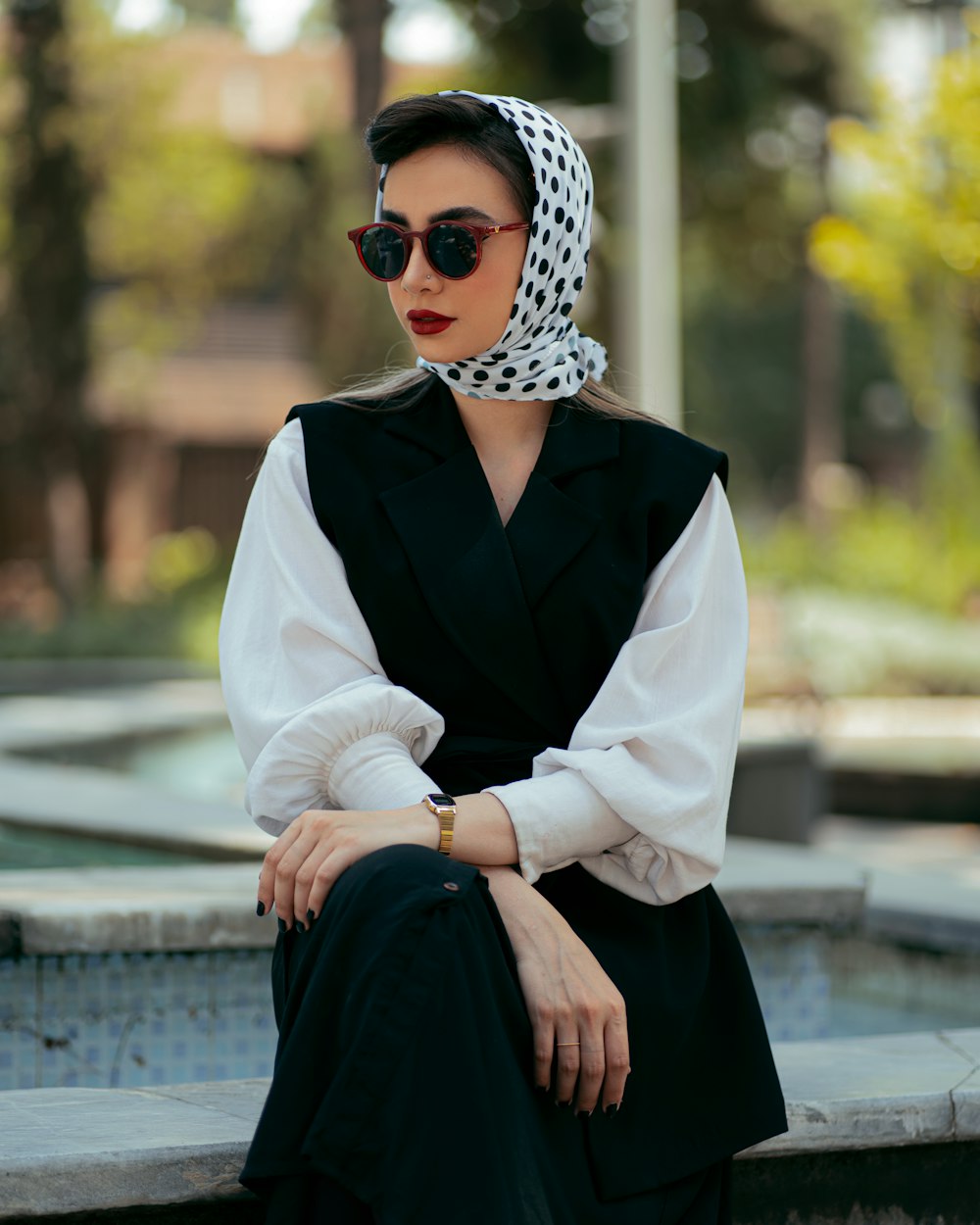 une femme assise sur un rebord portant des lunettes de soleil et un foulard