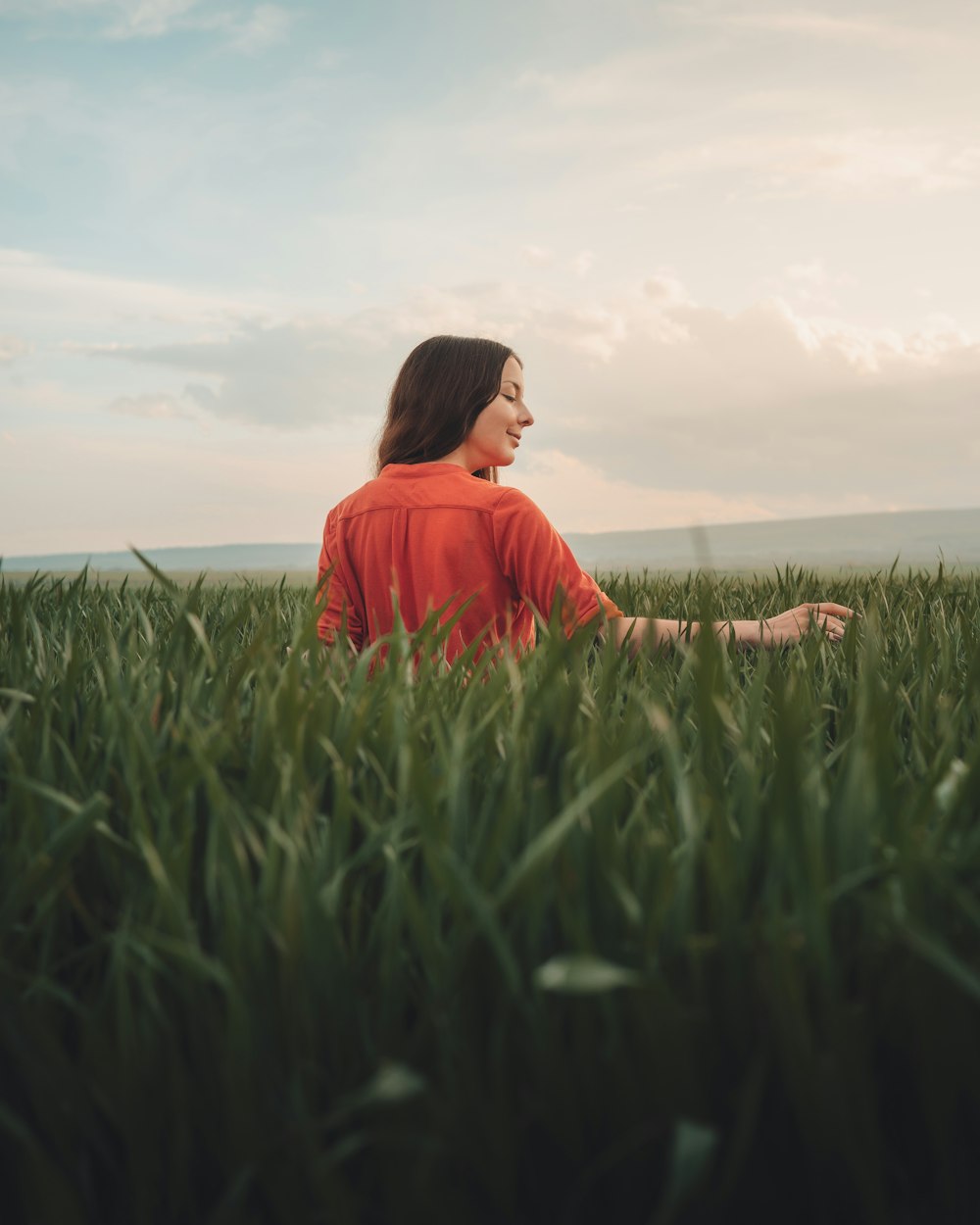 woman in red long sleeve shirt sitting on green grass field during daytime