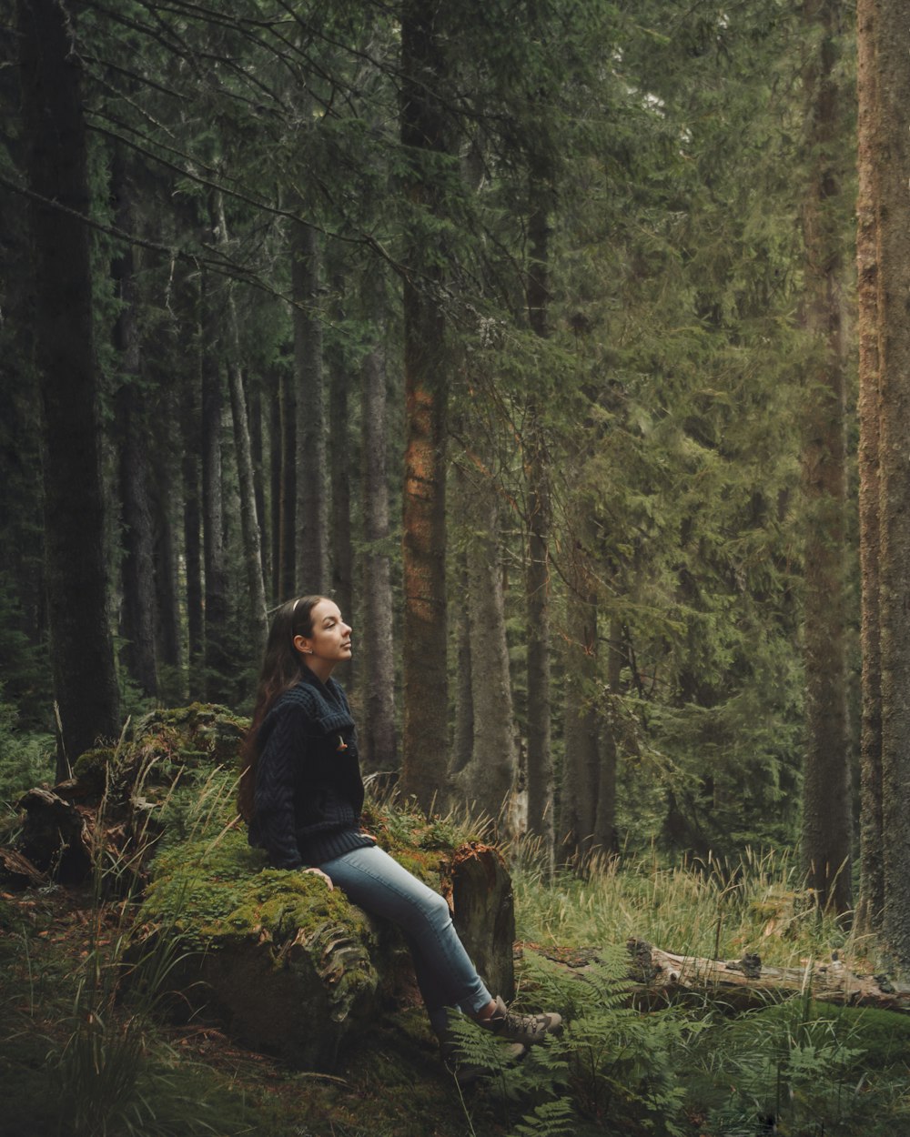 woman in black jacket and blue denim jeans standing on forest during daytime