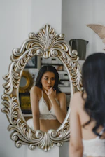 Elegant woman applying makeup in a soft pink-lit room reflecting beauty and confidence.