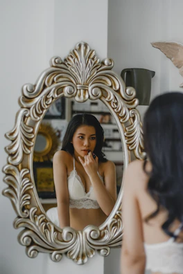 Smiling woman adjusting her Musa Latina corset in front of a vintage mirror.
