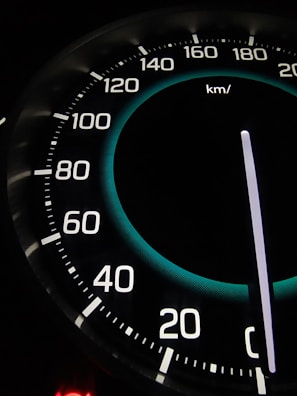 A close-up view of a car speedometer displaying speeds with increments from 20 to 220 kilometers per hour. The needle is pointing at zero, and there is a lit element indicating an empty or off state.