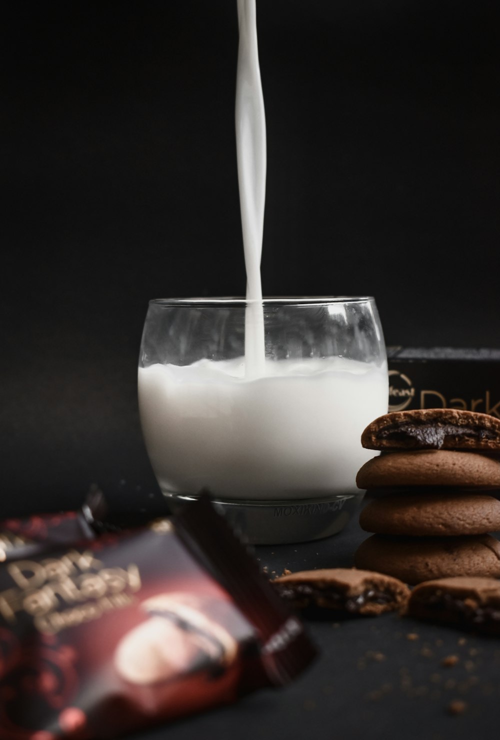 milk in clear drinking glass beside cookies on black plate