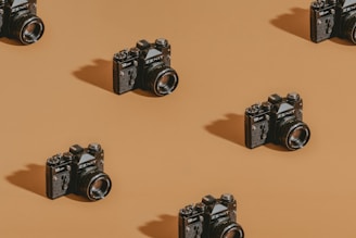Vintage cameras are neatly arranged in a repeating diagonal pattern on a warm brown background. The lighting creates shadows, adding depth and texture to the scene.