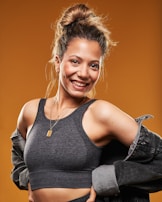 A joyful woman wearing a rosé-toned necklace, standing against a soft beige background, embodying confidence.