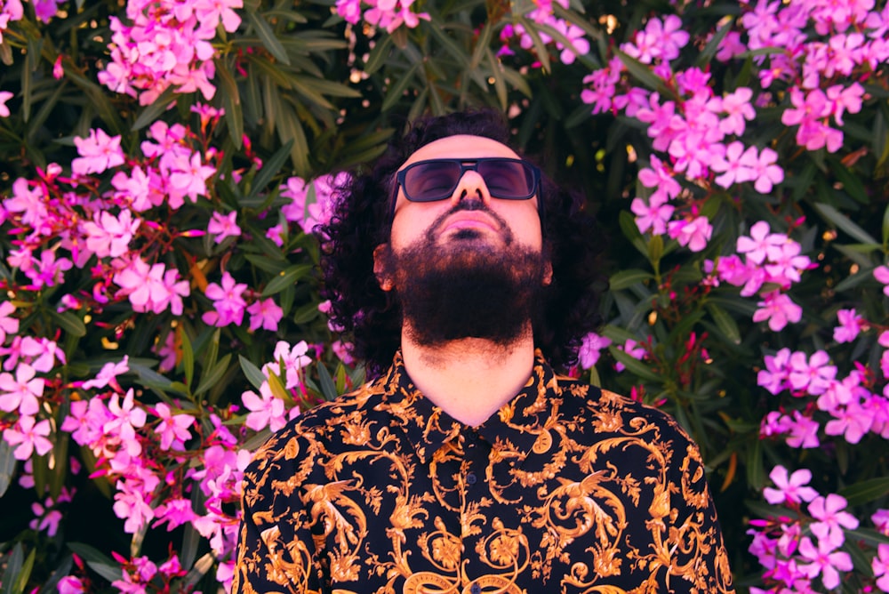 man in black and white floral shirt wearing black sunglasses standing near pink flowers