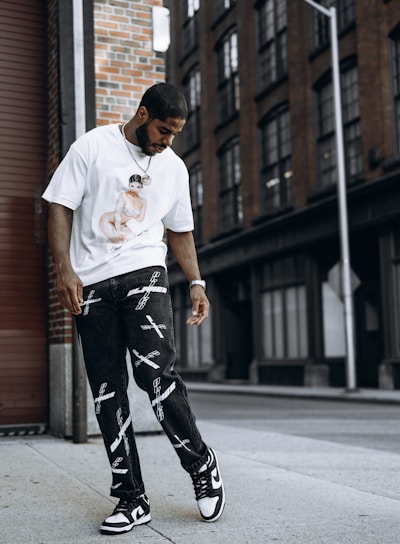 man in white crew neck t-shirt and black and white pants standing on sidewalk during