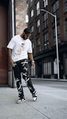 man in white crew neck t-shirt and black and white pants standing on sidewalk during