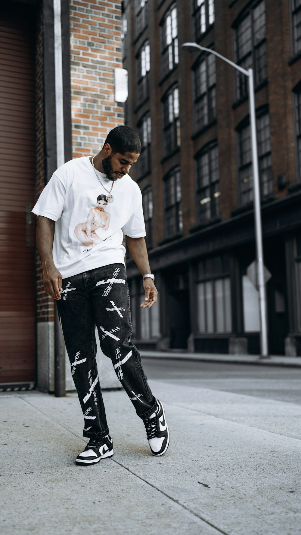 man in white crew neck t-shirt and black and white pants standing on sidewalk during