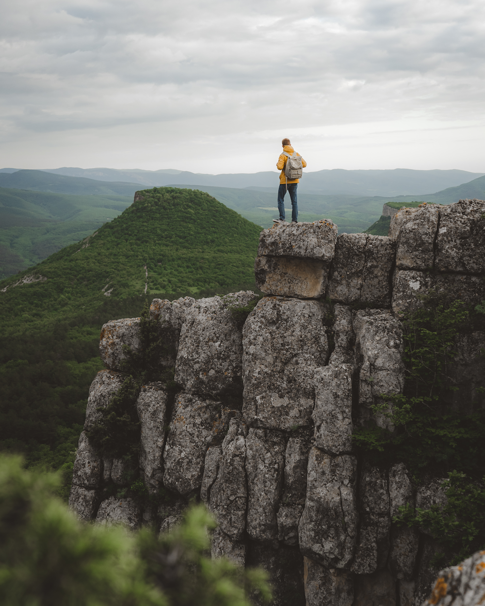 man in orange jacket standing on gray rock formation during daytime