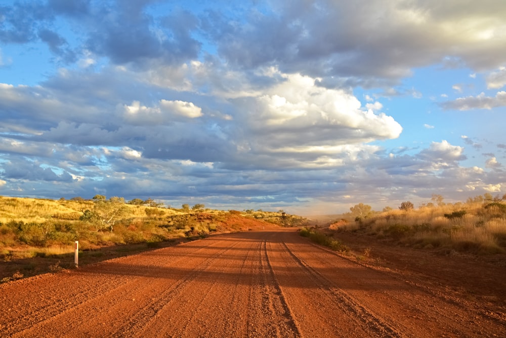 brown dirt road under blue sky and white clouds during daytime