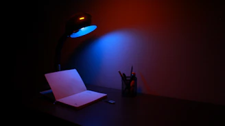 A sleek, dark-themed office desk with architectural blueprints and a glowing electric blue pen.