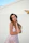 Elegant woman in a soft pastel outfit posing gracefully against a minimalist, light-filled backdrop