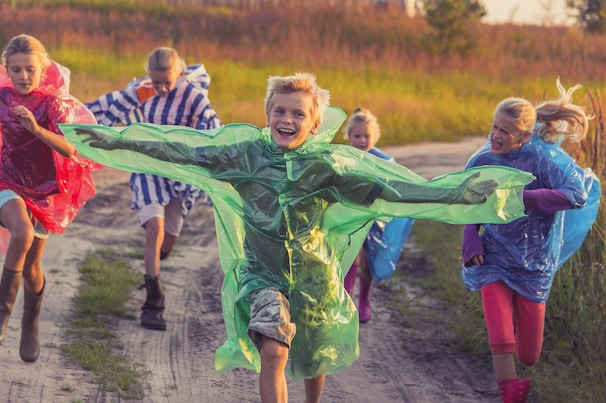 Children laughing together as they lead ponies along a leafy trail.