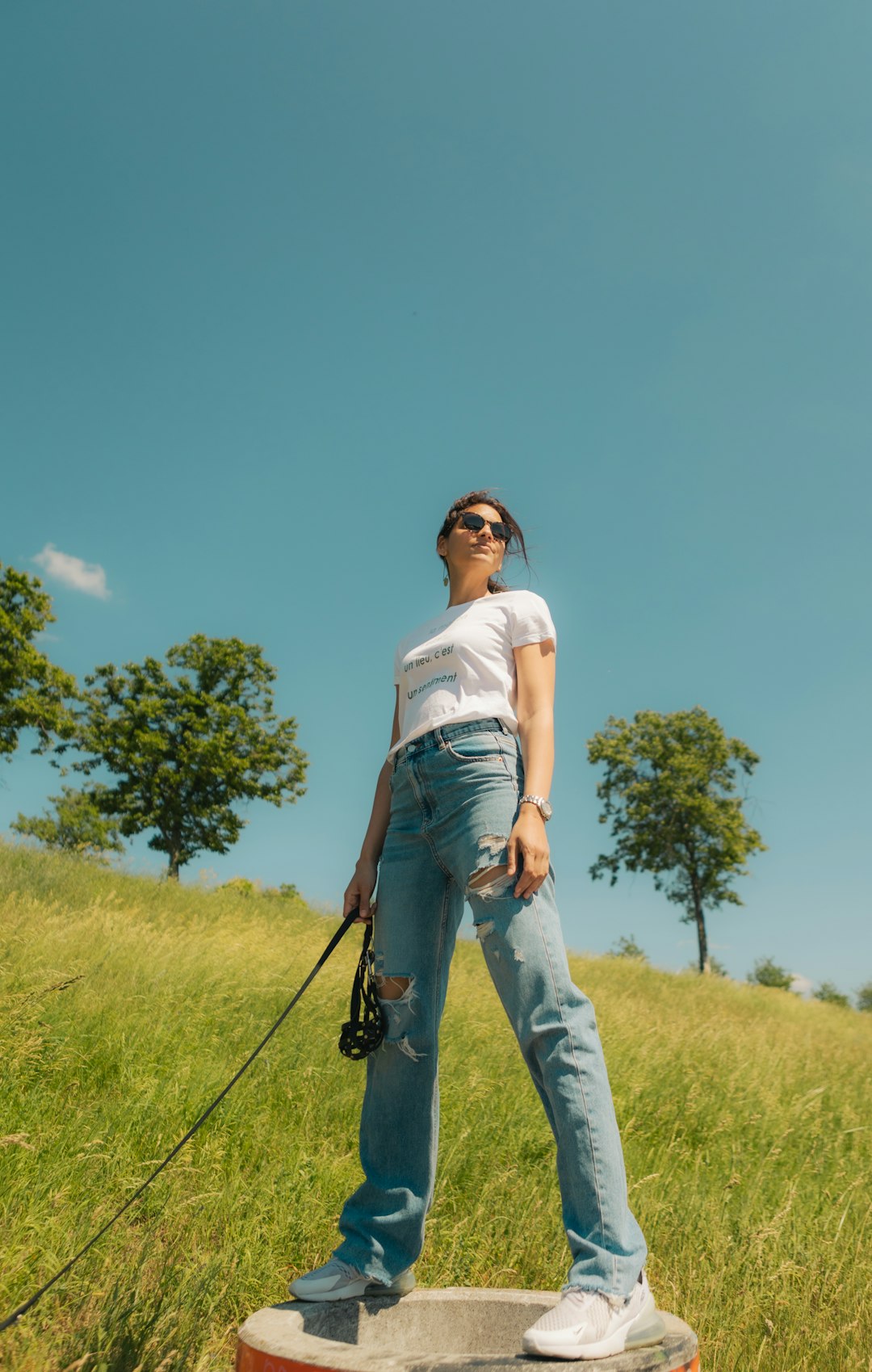 woman in white t-shirt and blue denim jeans standing on green grass field during daytime