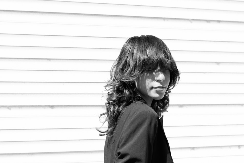 woman in black coat standing beside white wall