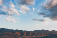 A serene landscape of rolling hills with patches of cultivated fields under soft sunlight.