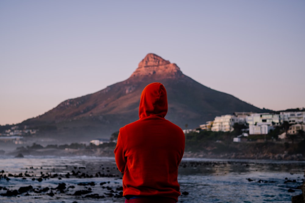 person in red hoodie standing on rock near body of water during daytime