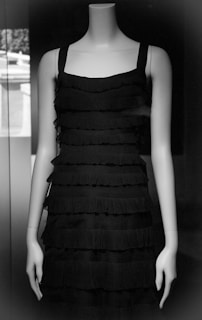 A sleek black blouse with subtle ruffle details shown on a mannequin in a bright studio